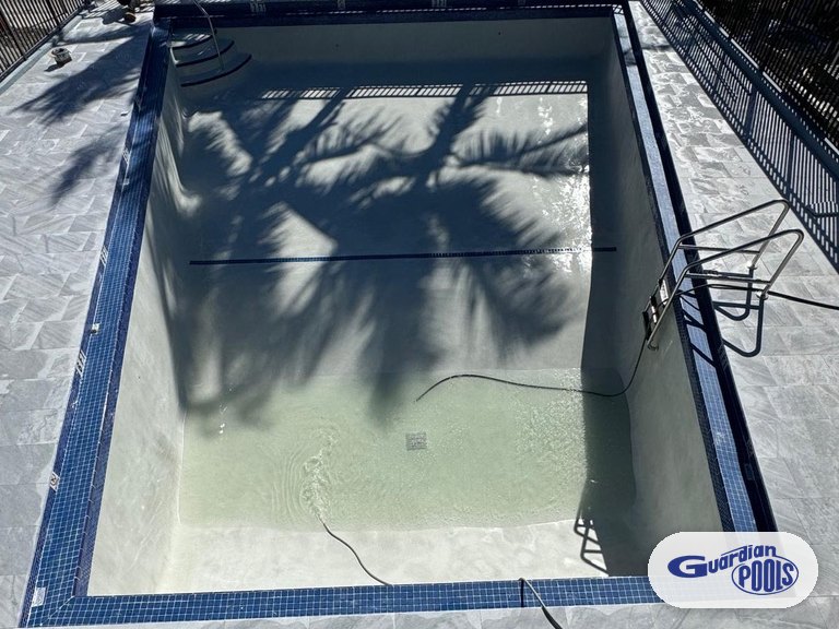 Drained condominium pool in Hollywood mid-renovation with blue waterline tile and a light stone deck